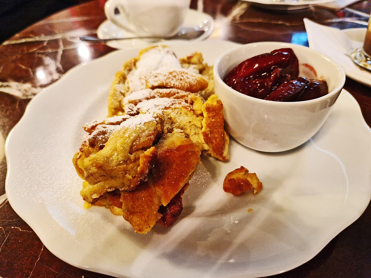 A plate of torn Kaiserschmarrn pancake dusted with icing sugar, served at a Viennese café