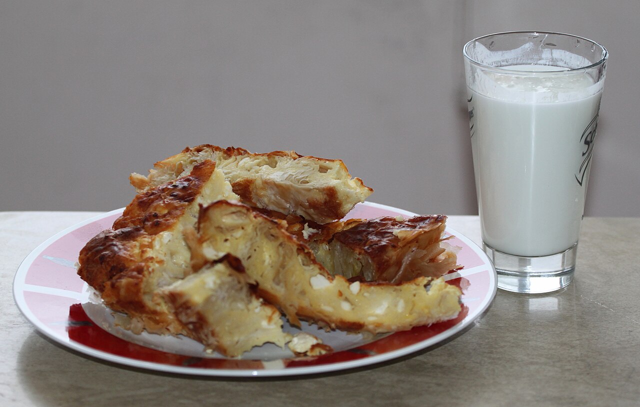 A slice of banitsa, flaky cheese pastry, served with a glass of yoghurt