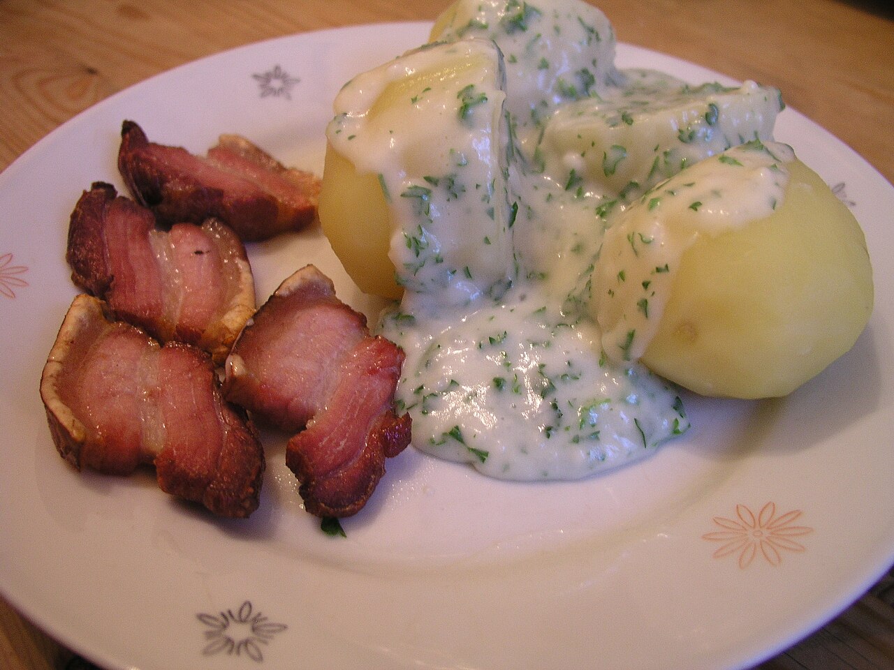 A plate of stegt flæsk, crisp slices of fried pork belly, with potatoes and parsley sauce