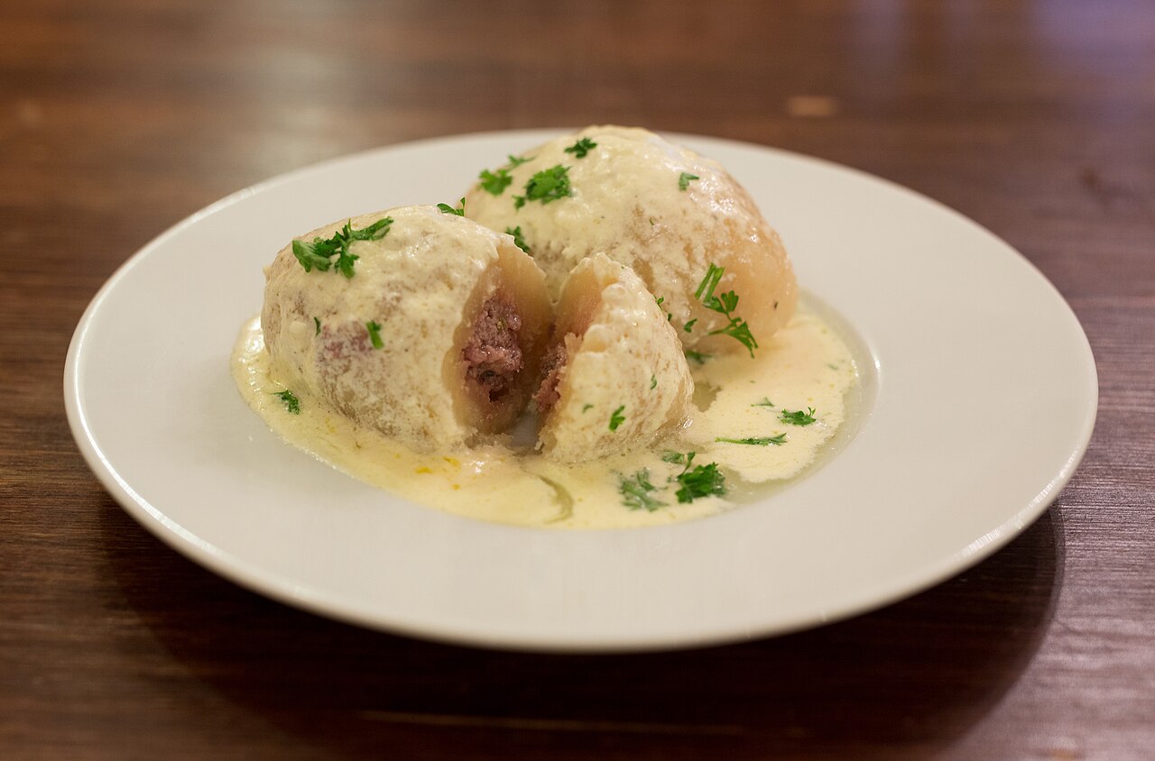 A plate of cepelinai, large potato dumplings, served with a sauce and bacon