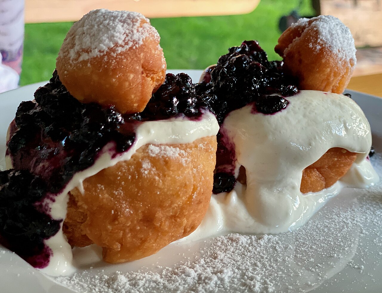 Fried dough balls dusted with icing sugar, topped with sour cream and dark berry jam, a plate of papanași