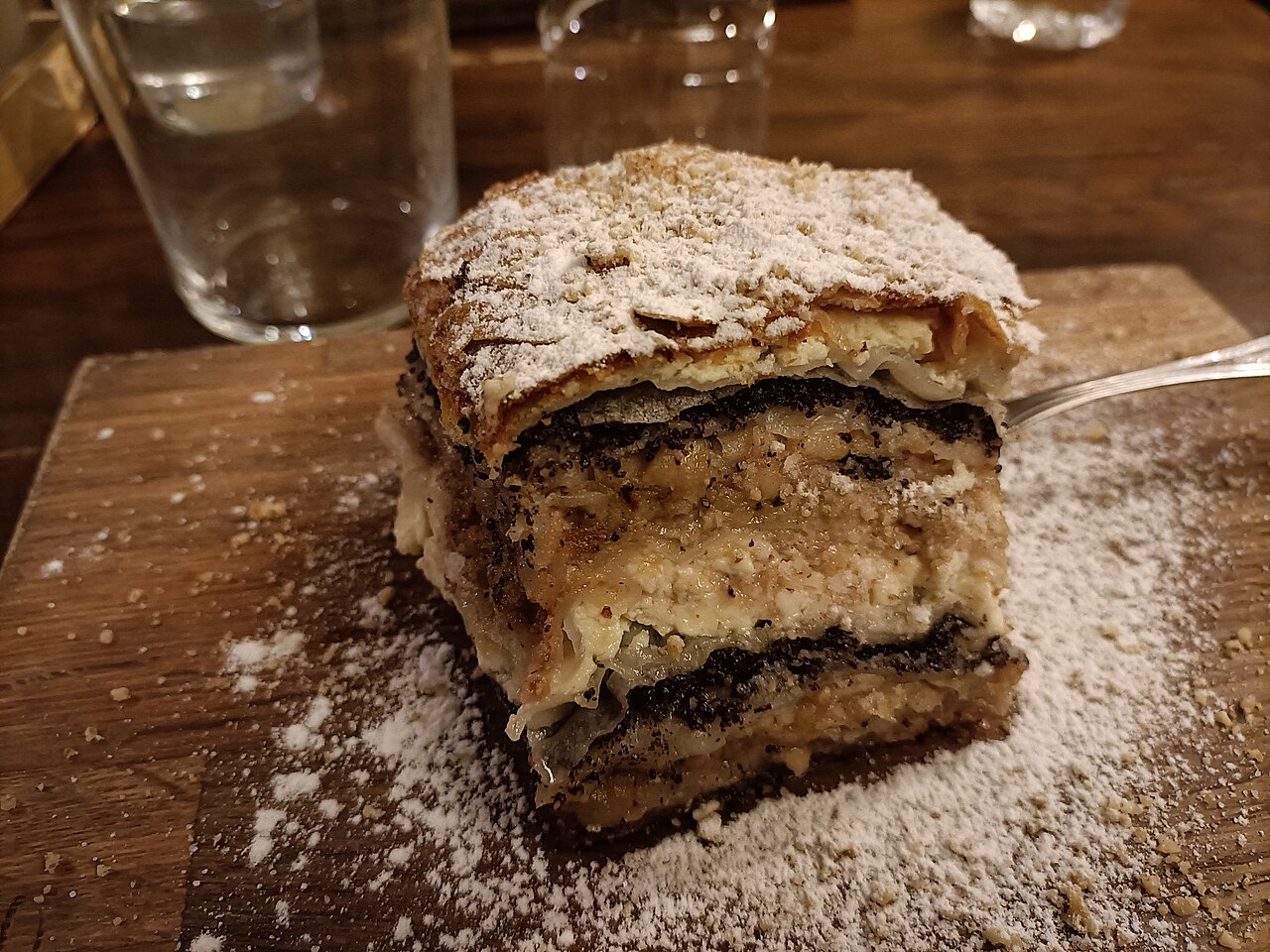 A slice of prekmurska gibanica, layered pastry with poppy seed, walnut, apple and curd, dusted with icing sugar