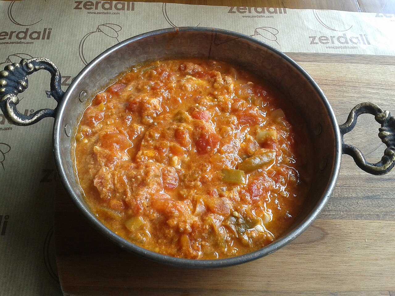Menemen, eggs cooked with tomato and peppers, in a copper pan on a wooden table