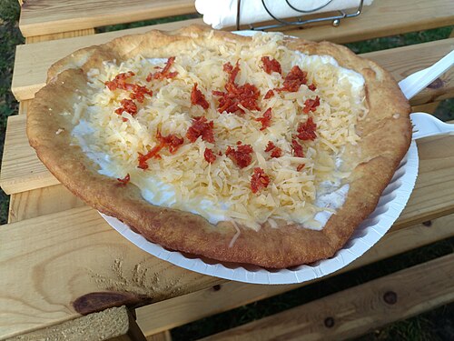 A fried lángos flatbread topped with sour cream and cheese