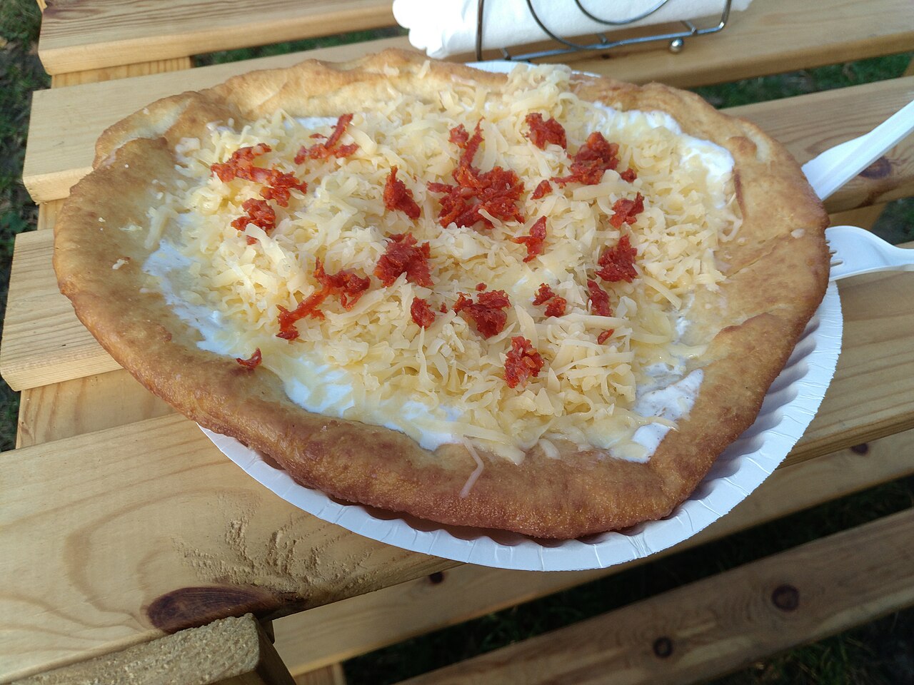 A fried lángos flatbread topped with sour cream and cheese