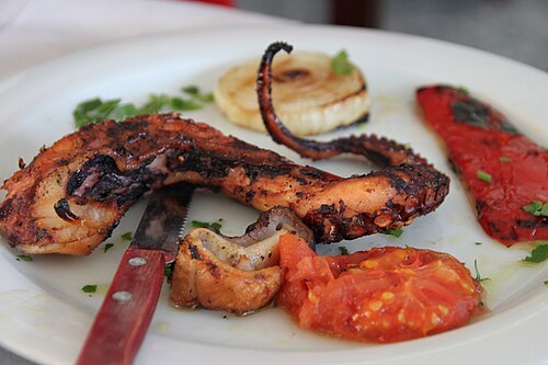 Charcoal-grilled octopus on a plate with grilled onion, pepper and tomato
