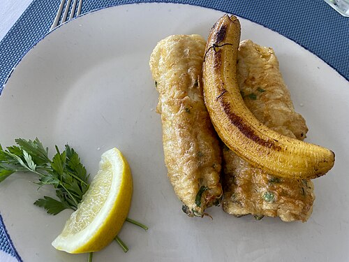 Two fried black scabbardfish fillets with a grilled banana and a lemon wedge on a white plate