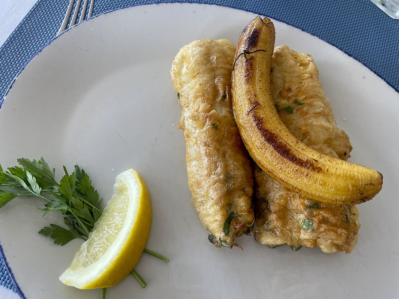 Two fried black scabbardfish fillets with a grilled banana and a lemon wedge on a white plate