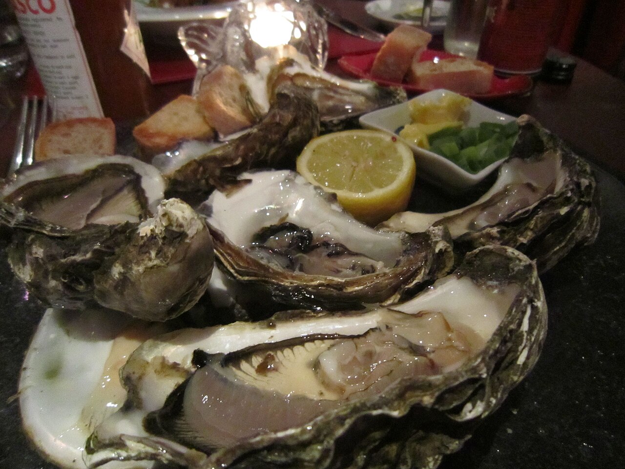 A plate of open oysters on the shell with a lemon wedge and brown bread at the side