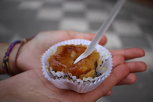 A pionono, a small rolled sponge cake with a toasted cream top, in a paper case held in one hand