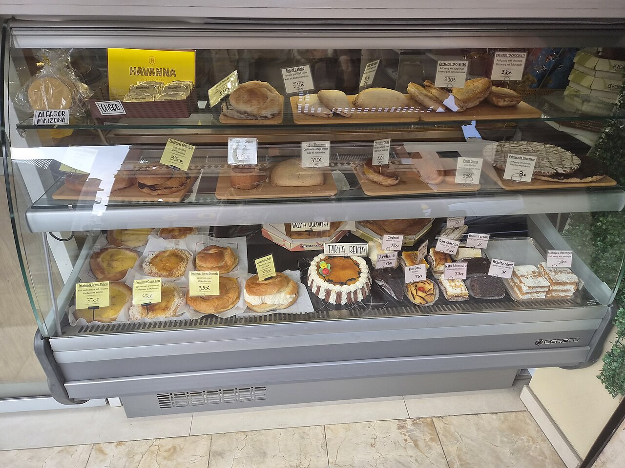 A glass display case in a Palma bakery holding ensaïmadas, pastries and cakes