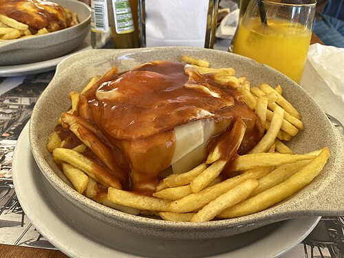A francesinha sandwich covered in sauce and cheese on a plate
