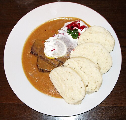 A plate of svíčková na smetaně with sliced beef, cream sauce and bread dumplings
