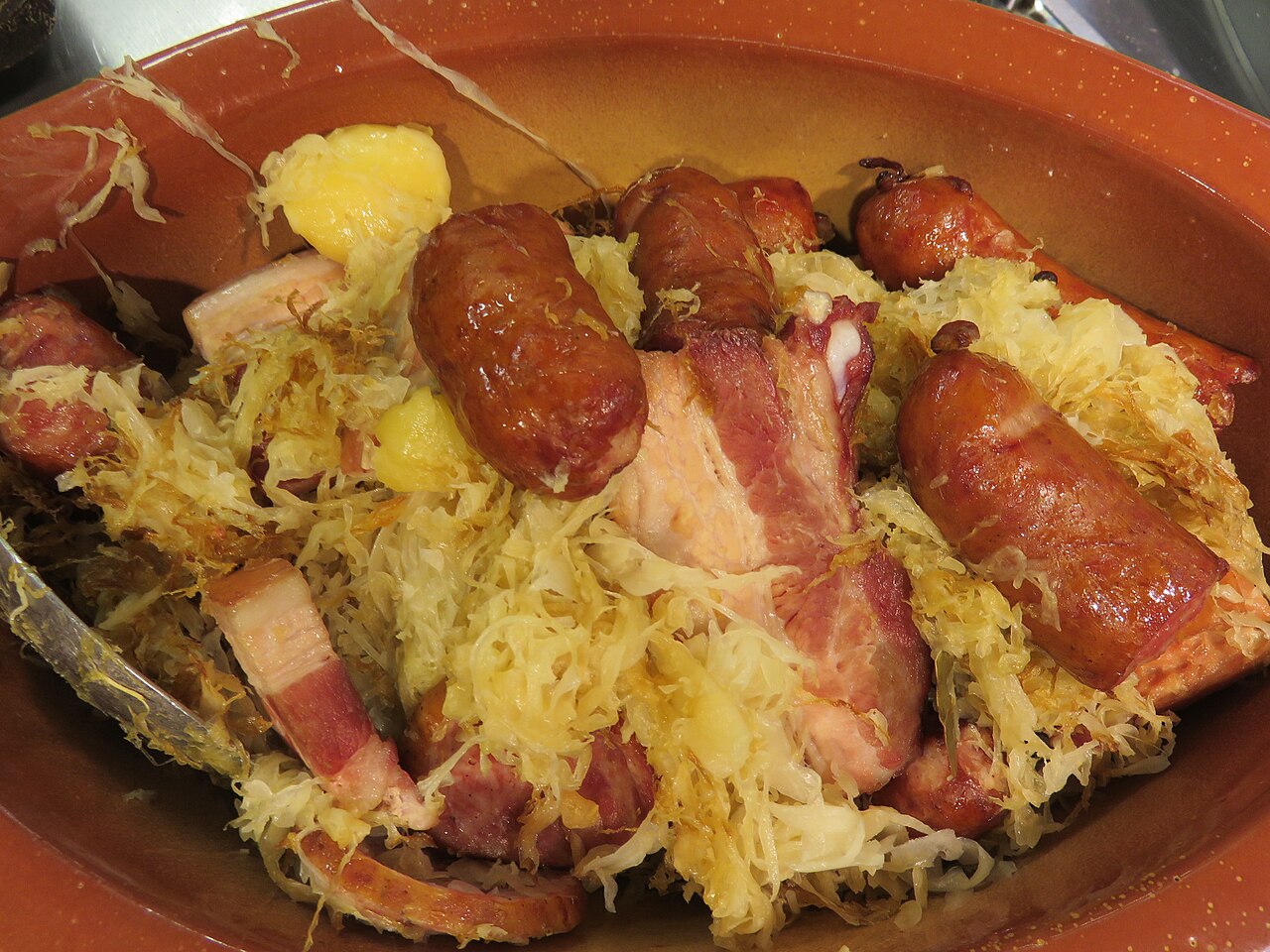 Choucroute garnie in a terracotta dish: sauerkraut with sausages, pork belly and potatoes