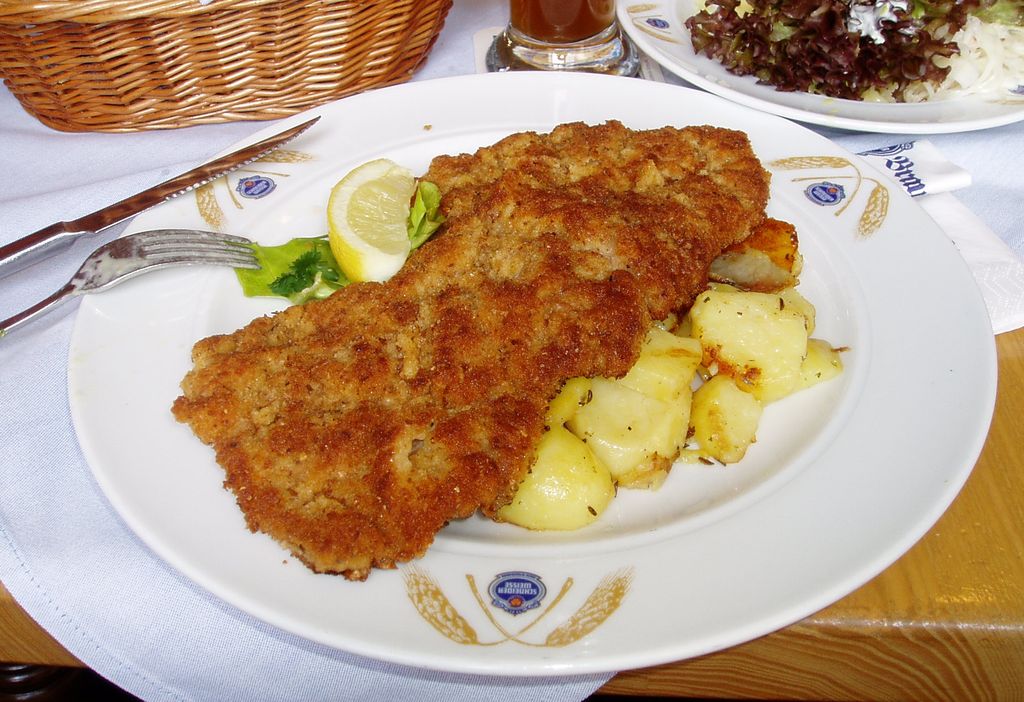 A breaded Wiener Schnitzel with a lemon wedge and potato salad on a plate