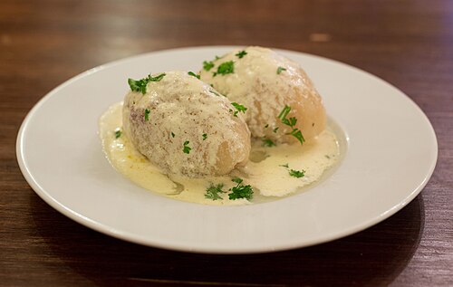 Two cepelinai, Lithuanian potato dumplings, on a white plate under a cream sauce with chopped parsley