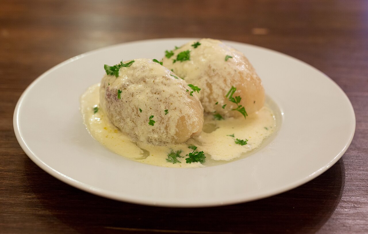 Two cepelinai, Lithuanian potato dumplings, on a white plate under a cream sauce with chopped parsley