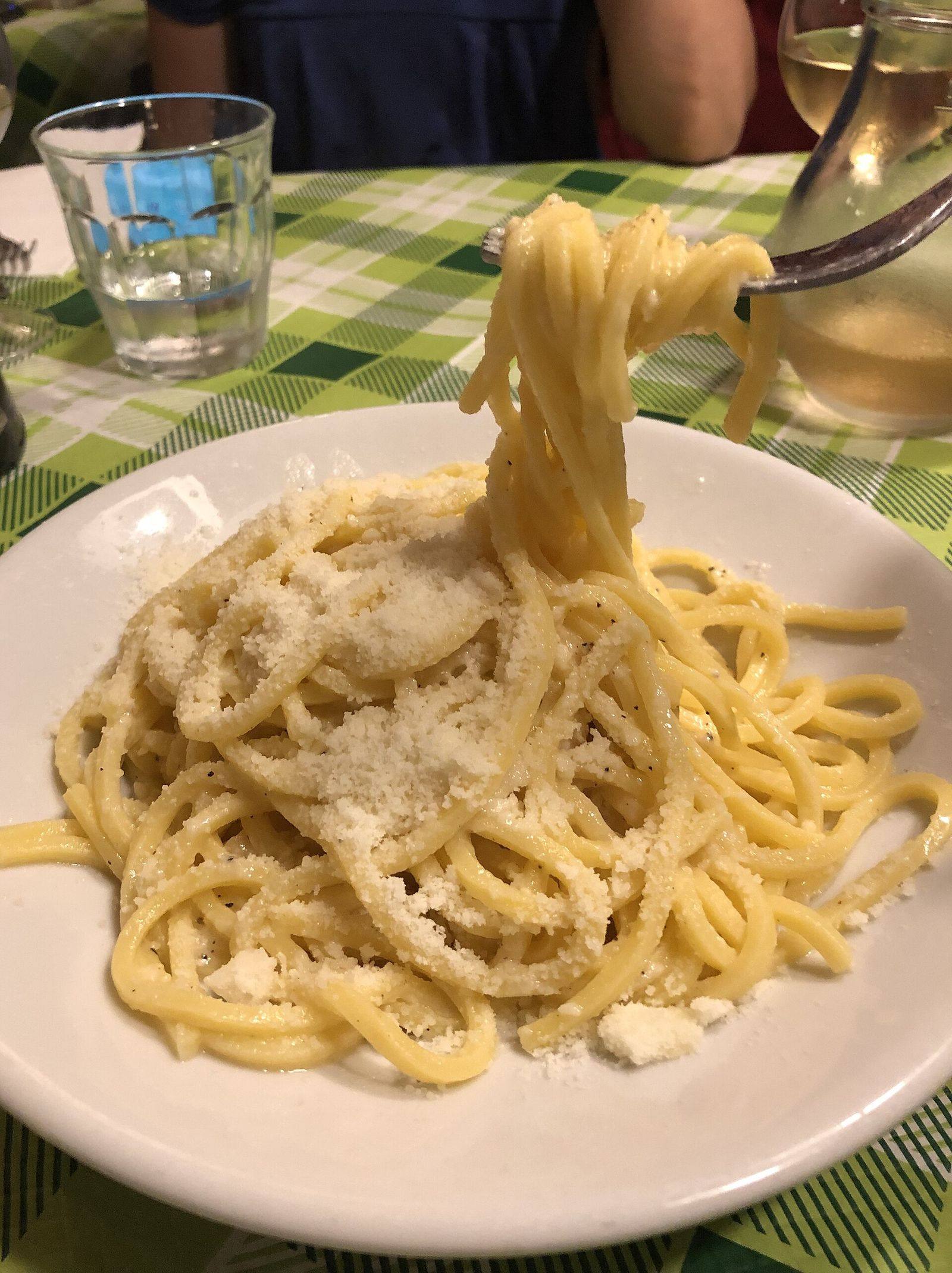 A forkful of spaghetti cacio e pepe lifted from the plate, on a green checked tablecloth in a Rome trattoria